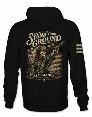 A black pullover hoodie shown from the back, featuring a large distressed graphic print of a skeleton cowboy holding a revolver with the text 'Stand Your Ground' and 'Allegiance Est. 2011'.